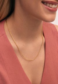 Collar de cadena de oro con eslabones ovalados, de textura plana, descansando sobre un cuello desnudo, combinado con una blusa de tela de color rosa suave.
