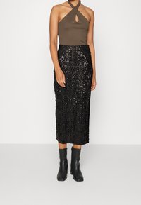 Body s halter výstřihem v olivově zelené barvě, doplněný černou sukní tužkového střihu s flitry a přiléhavým střihem. Kombinováno s černými kotníkovými botami.