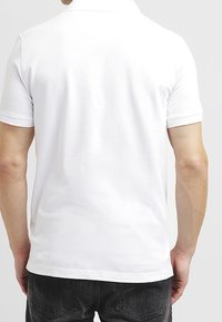 Polo blanc à manches courtes avec un col plat, présentant une texture lisse et une coupe décontractée, vu de dos.