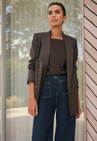 Double-breasted dark brown blazer with glossy buttons, paired with a dark top and high-waisted wide-leg blue jeans. Clean, tailored design.