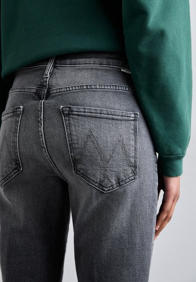 Jeans in denim grigio con una forma aderente, dotati di due tasche posteriori e un motivo a zigzag. Indossati con una felpa verde in vita.