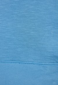 Tela azul claro con una superficie suave y texturizada. Presenta un patrón de punto uniforme y una costura ordenada a lo largo del dobladillo y los bordes.