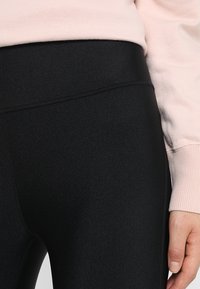 Lähikuva henkilöstä, joka on pukeutunut vaaleanpunaiseen huppariin ja mustiin legginsseihin, korostaen vaatteen kangasta ja istuvuutta.