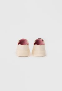 Une paire de sneakers ivoire avec des semelles épaisses et des languettes en velours rose profond, vues de l'arrière sur fond blanc uni.