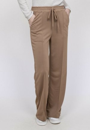 Pantalon marron à coupe ample avec poches avant et taille à cordon, porté avec des baskets blanches et un haut à manches longues gris clair.