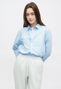 Γαλάζιο πουκάμισο με κουμπιά και γιακά, στενά μανίκια και άνετη εφαρμογή, συνδυασμένο με ανοιχτό γκρι φόρμα με ελαστική μέση.