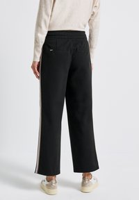Svarta vida sweatpants med elastisk midja, med sidolinjer i ljusa färger och en bakficka. Slät tygtextur.