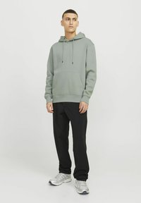 Un sweat à capuche vert clair avec une poche kangourou, un capuchon à cordon réglable, des poignets côtelés, associé à un pantalon de jogging noir et des baskets de course argentées.