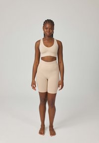Beżowy sportowy biustonosz z cienkimi ramiączkami i krótkim krojem, zestawiony z beżowymi szortami o wysokim stanie. Gładka faktura, dopasowany krój.
