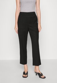 Pantalons noirs avec une coupe décontractée, une taille élastique et des jambes droites. Portés avec un débardeur gris et des sandales à talons noires.