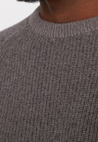 Grauer Strickpullover mit gerippter Textur, ausgestattet mit einem einfachen Rundhalsausschnitt und einer enganliegenden Passform, die gleichmäßige Nähte aufweist.