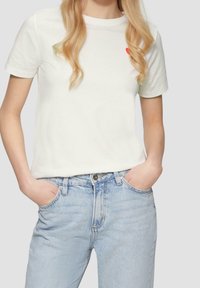 Hvid bomulds t-shirt med rund halsudskæring og et lille rødt hjerte designet på brystet, parret med lyseblå denim jeans.