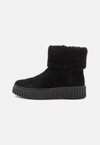 Botas de tobillo negras de ante con un puño de piel sintética y una suela de goma gruesa y acanalada. Presenta una puntera redondeada y detalles de costura mínimos.