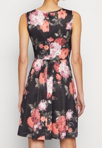 Svart blommig klänning med ärmlös design, med stora rosa och korallblommor, figurnära bodice och utsvängd kjol. Slät tygliknande textur.