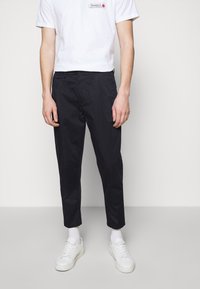 Zwarte taps toelopende broek van een katoenmix, met voorzakken, gecombineerd met witte sneakers en een wit T-shirt met opdruk.