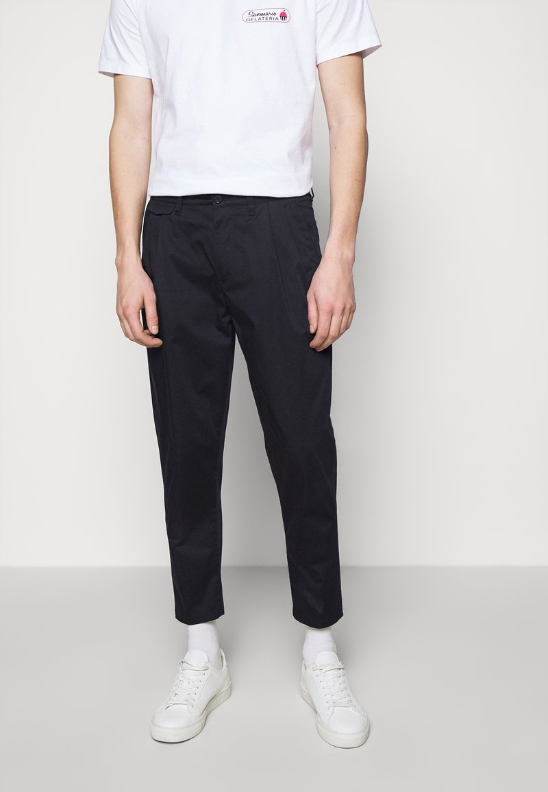 Zwarte taps toelopende broek van een katoenmix, met voorzakken, gecombineerd met witte sneakers en een wit T-shirt met opdruk.