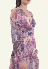 Floral wrap dress in sheer fabric featuring pink, purple, and orange patterns. Long sleeves with elastic cuffs and a deep v-neckline.