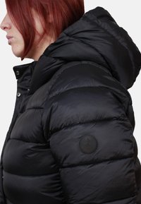 Zwarte pufferjack met een capuchon, met een geborduurde ontwerp, glanzende textuur en een cirkelvormig logo op de linkermouw.