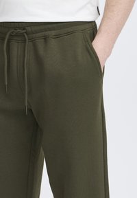 Joggingbukser i olivengrøn lavet af blødt stof, med justerbar snor i taljen og sidelommer.
