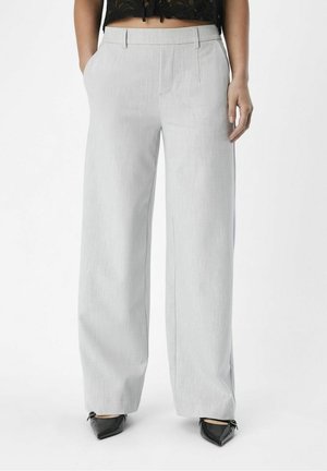 Hellgraue, weit geschnittene Hosen mit strukturiertem Stoff, ausgestattet mit Vordertaschen und tailliertem Schnitt. Kombiniert mit schwarzen spitzen Schuhen.