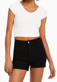 Vit kortärmad croppad topp med v-ringning, kombinerad med högmidjade svarta denimshorts med knappstängning och sidfickor.