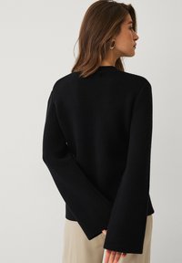 Zwarte gebreide trui met een ronde hals, wijde mouwen en een geribbelde stof. Heeft een strak ontwerp zonder zichtbare versieringen.