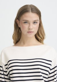 Pull léger en crème avec des rayures horizontales bleu marine, encolure large et coupe décontractée. Fabriqué en tissu tricoté doux, avec des manches longues.