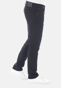 Jeans de mezclilla negra con corte ajustado, que cuentan con un clásico diseño de cinco bolsillos y una cinturilla texturizada con un parche de cuero.