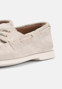 Μπεζ σουέντ παπούτσι τύπου boat με εσωτερική επένδυση από δέρμα, λεπτομέρειες με κορδόνια και λευκή λαστιχένια σόλα σε ουδέτερο φόντο.