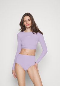 Fialový crop top s dlhým rukávom a vysokoštíhlým bikínovým spodkom, vyrobený z elastického materiálu, s jednoduchým dizajnom a logom na topu.