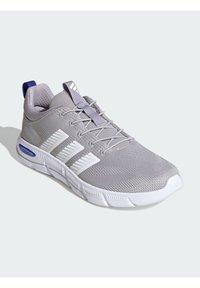 Svetlo šedá športová obuv s priedušným sieťovaným zvrškom, bielou podrážkou, nápadným dizajnom s tromi pruhmi a fialovým pätovým dielom. Textúrované akcenty po celom obvode.