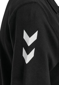 Zwarte poloshirt met gestructureerde stof. Heeft drie witte chevronstrepen op de bovenkant van de mouw. Klassieke kraag en knoopsluiting.