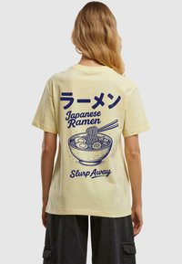 Žluté bavlněné tričko s modrou grafikou mísy ramen, hůlek a japonského textu. Jednoduchý design s volným střihem.