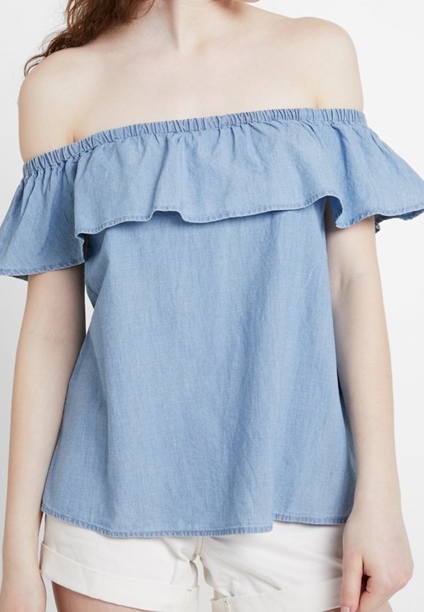 Světle modrý top bez ramínek s volánovým výstřihem, vyrobený z jemného denimu. Volný střih s krátkými rukávy a rovním lemem.