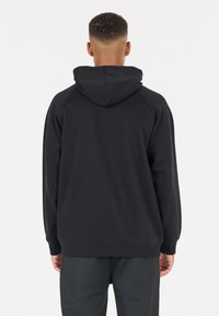 Svart hoodie med dragsko, raglanärmar och ribbade muddar. Har en mjuk textur och en enkel, ren design.