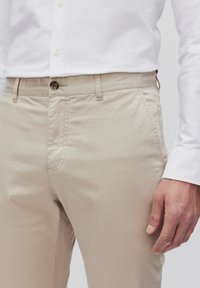 Beige chino's met een slim fit. Gemaakt van lichtgewicht stof, met voorzakken en een knoopsluiting. Gecombineerd met een witte overhempt.