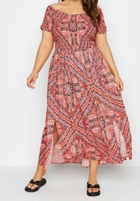 Maxiklänning i röd med svart och vit paisley-mönster; axelbandslös design, korta ärmar och sidoflikar för rörelsefrihet.