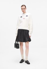 Lun hvit genser med katt ansiktsdesign, svart satengskjørt, svart håndveske, lys beige sokker, og svarte loafers med nagler.