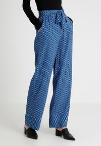 Blå mönstrade vida byxor med knytmidja, med ett diamantmönster i vitt och ljusblått. Tillverkade av ett lätt tyg.