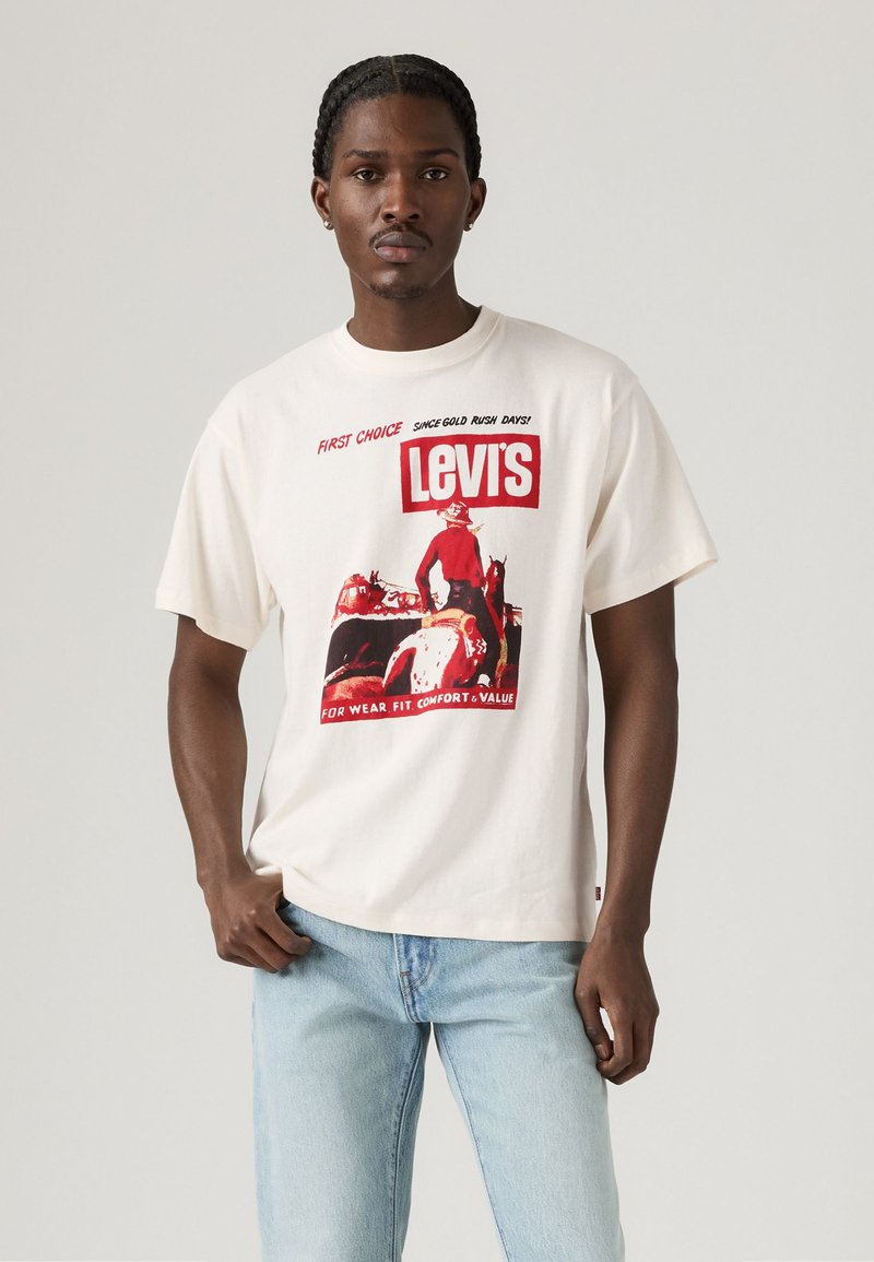 Witte katoenen t-shirt met een rode grafische afdruk van een cowboy, "Levi's" tekst en een boxy fit. Gecombineerd met lichtblauwe denim jeans.