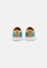 Une paire de baskets basses avec des panneaux bleus et beige, des semelles blanches, montrées de l'arrière sur un fond blanc.