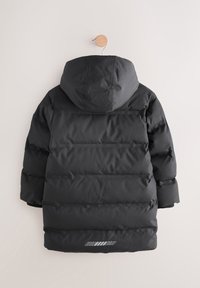 Doudoune noire avec capuche, dotée de panneaux horizontaux, de poignets côtelés et d'une bande réfléchissante à l'ourlet. Matière lisse et résistante à l'eau.