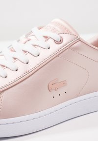 Light pink satin sneaker with white laces, featuring a smooth surface and subtle logo detail. Textured white rubber sole for grip.