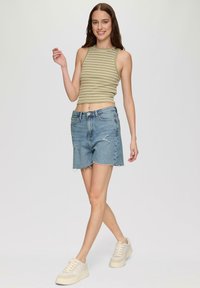 Zielono-biały w paski top crop, dżinsowe szorty z postrzępionymi brzegami, jasnoniebieskie, swobodne sneakersy z off-white akcentami, model w pozie spacerowej.