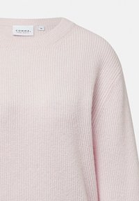 Jasnoróżowy sweter z dzianiny o żebrowej fakturze, okrągłym dekolcie i metce z nazwą marki oraz rozmiarem.