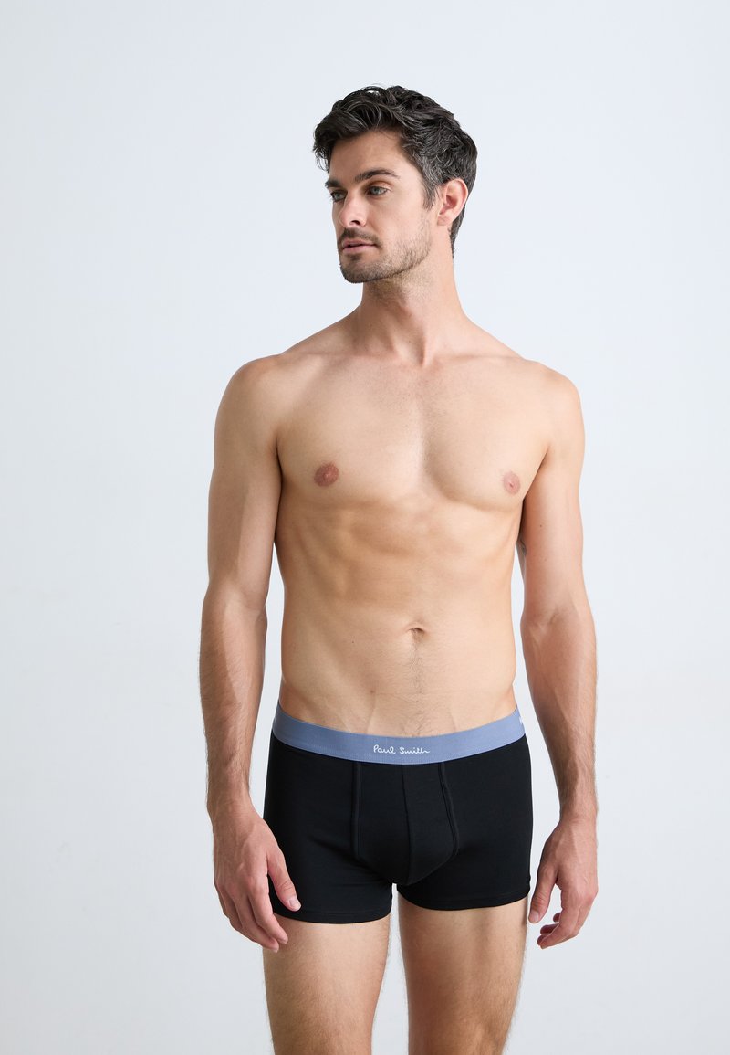 Boxer-briefs noirs avec une ceinture élastique bleu clair. La ceinture présente un texte blanc. Le tissu semble lisse et extensible.