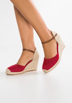 Røde ruskinds kilehæl espadriller med hæl af flettet jute, der har en brun ankelrem og rundet tådesign. Glat tekstur og robust konstruktion.