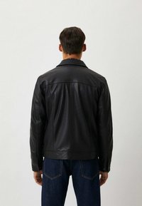 Zwarte leren jas met een gladde textuur, klassieke kraag en slim-fit pasvorm. Voorzien van gestikte details op de schouders en mouwen.