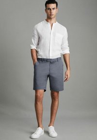 Vit linneskjorta med krage, en bröstficka, tillsammans med grå shorts och vita sneakers. Avslappnad outfit i neutrala färger.