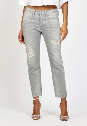 Gray distressed slim-fit jeans worn with snakeskin high-heeled sandals and a cropped white top, showing legs and midriff.
